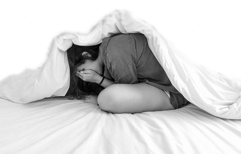 woman hiding under duvet cross legged with head in her hands