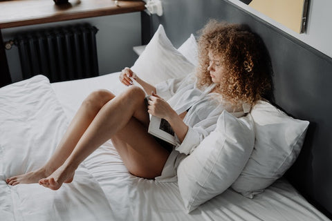 lady lying in bed with her back on pillows reading