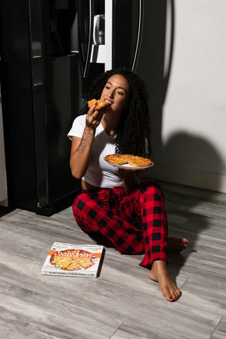 lady eating pizza next to fridge in pyjamas